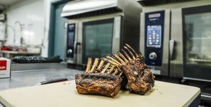 Cooked rack of lamb on a cutting board in front of RATIONAL iCombi Pro combi ovens.