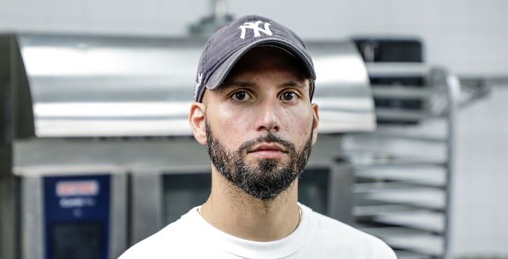 Chef in a white shirt and cap standing in front of a RATIONAL iCombi Pro combi oven in a commercial kitchen.