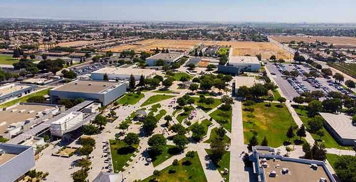 Aerial view of a sprawling campus with multiple buildings surrounded by green spaces, located next to an expansive undeveloped land area.