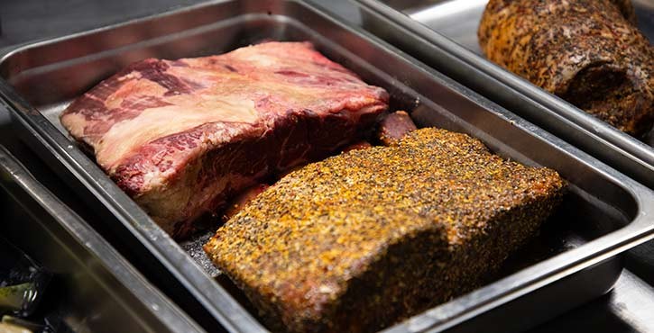 A close-up of two cuts of beef, one marbled and the other seasoned, displayed in a tray.