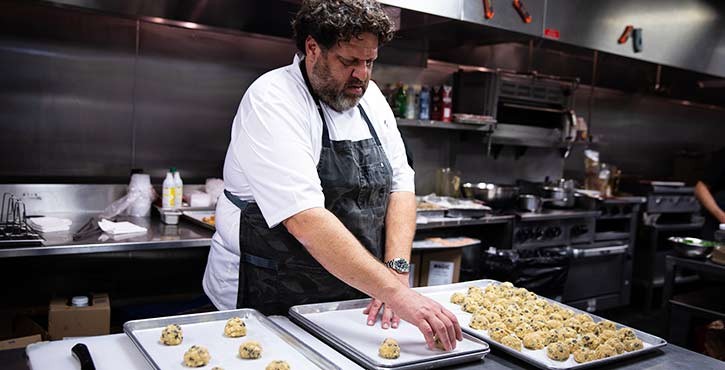 A chef carefully shaping dumplings on baking trays in a busy kitchen.