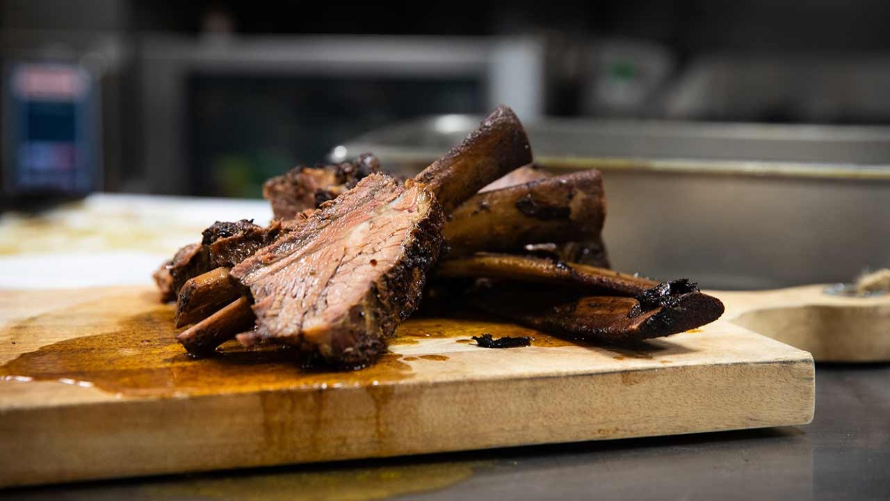 A close-up of a wooden cutting board displaying beautifully cooked beef ribs with a savory glaze.