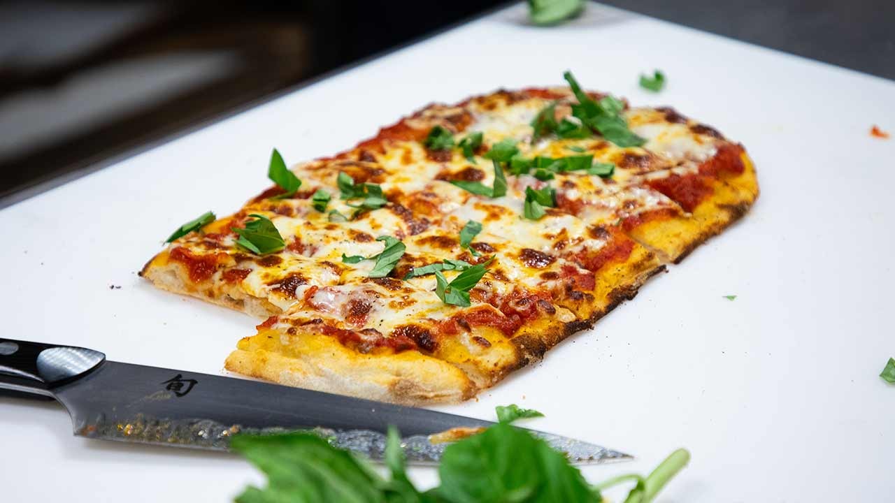 A freshly baked pizza topped with cheese and fresh basil, resting on a cutting board next to a knife.