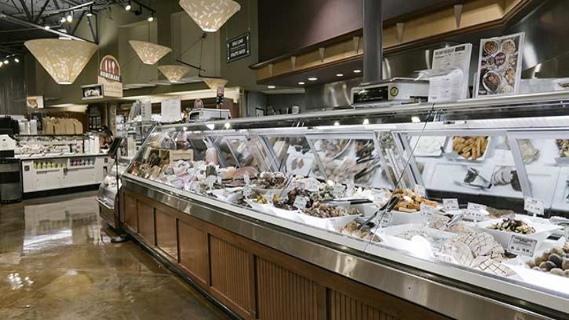 Interior view of a Whole Foods Market bakery section, showcasing a variety of breads, pastries, and other baked goods displayed in large glass cases under overhead lighting.