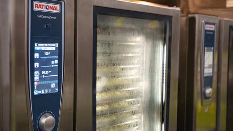 A row of Rational SelfCookingCenter ovens in a commercial kitchen, focusing on the digital control panel of the nearest oven.