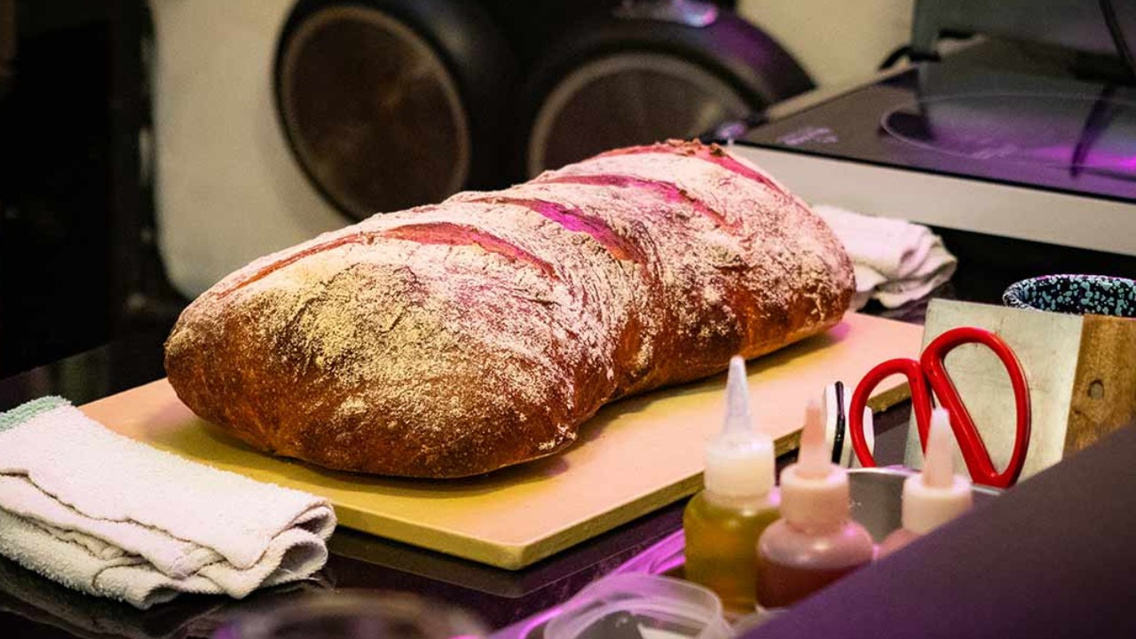 A freshly baked loaf of bread rests on a cutting board, surrounded by kitchen utensils and a cozy atmosphere.