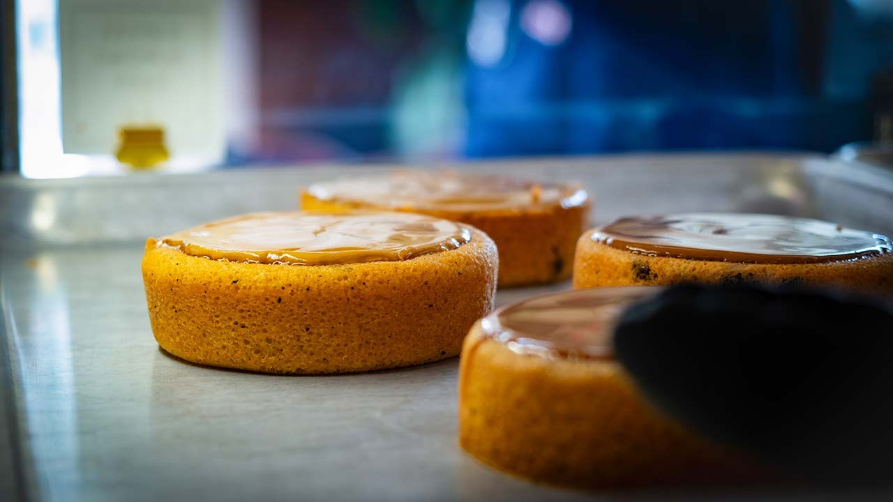 Close-up of freshly baked cakes with a glossy topping, arranged on a baking tray.