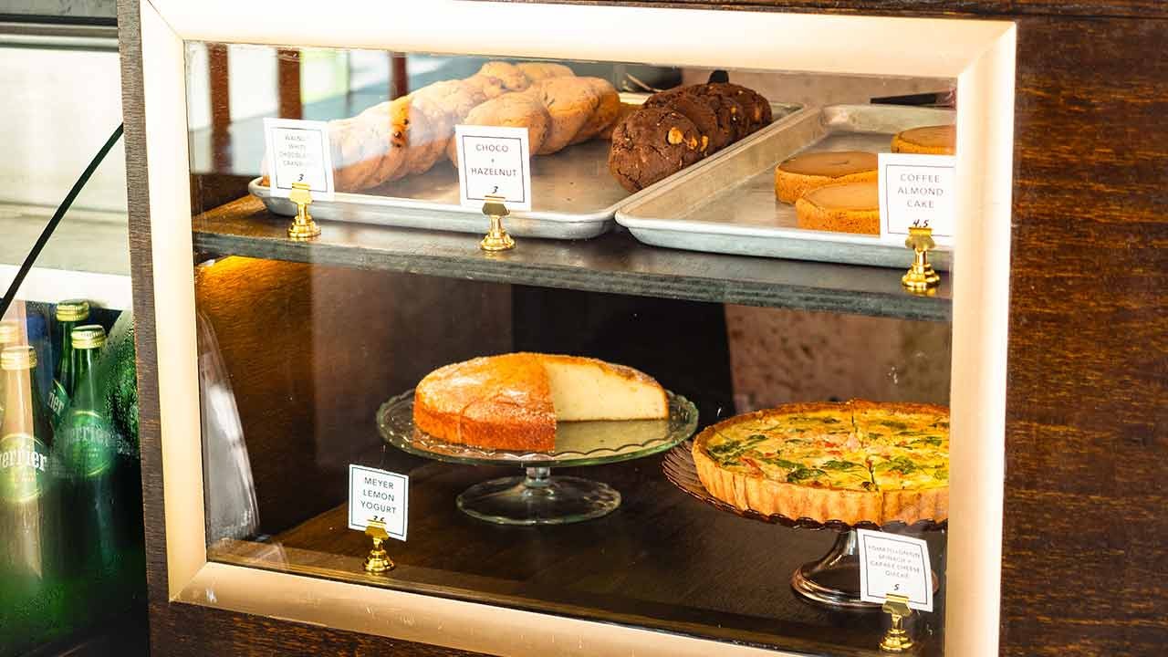 A display case filled with various baked goods, including cookies, cakes, and tarts, with price labels visible.