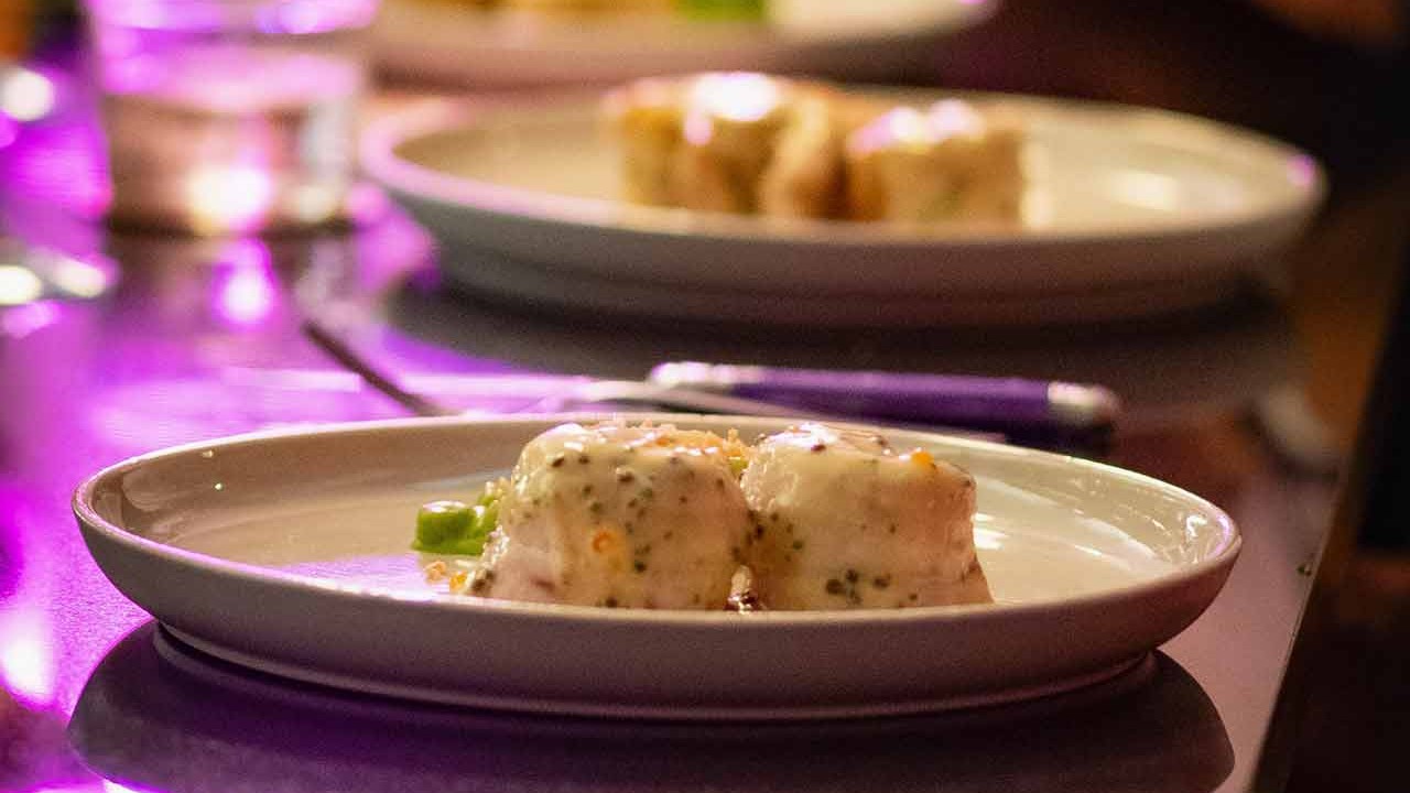 A plate of food featuring two creamy dumplings topped with sauce and garnished, set against a colorful backdrop.