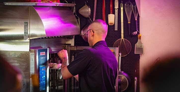A chef adjusts the settings on a high-tech iCombi Pro oven in a colorful kitchen environment.
