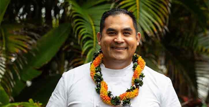 Smiling man wearing a colorful flower lei in a tropical garden.
