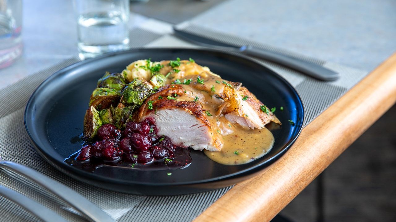 Roast chicken with gravy, Brussels sprouts and cranberry sauce served on a black plate.