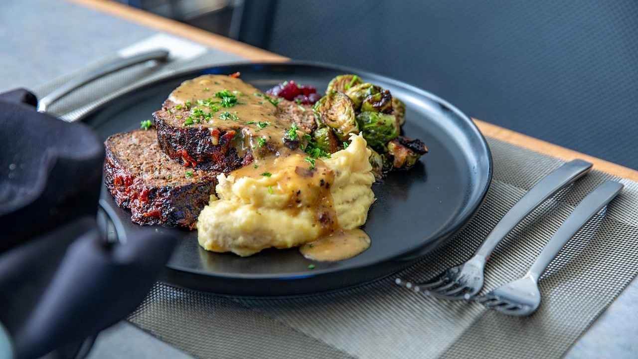 Meatloaf with gravy, mashed potatoes and roasted Brussels sprouts on a black plate.