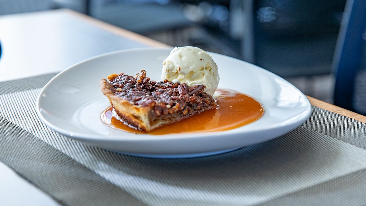 Slice of pecan pie with vanilla ice cream and caramel sauce on a white plate.