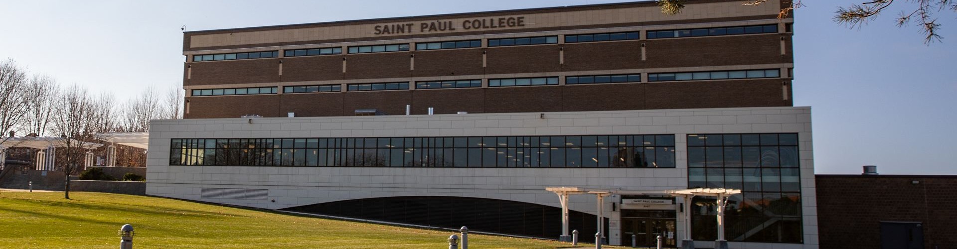 Exterior of Saint Paul College with modern campus building, lawn and trees under a clear sky.