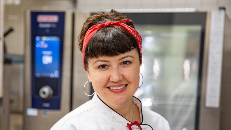 Smiling culinary instructor in a white chef’s coat stands in front of a RATIONAL iCombi Pro combi oven.