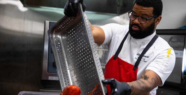Chef in red apron pouring cooked lobster from a perforated tray.