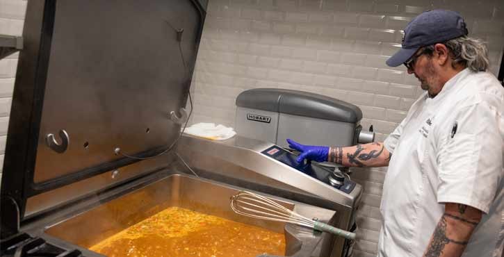 Chef adjusting RATIONAL iVario Pro while cooking stew in a professional kitchen.
