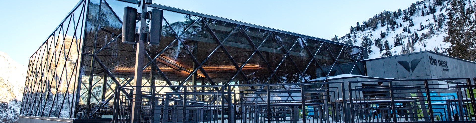 Modern glass restaurant building in snowy mountains with outdoor terrace at The Nest at Snowbird.