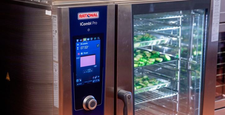 Close-up of a RATIONAL iCombi Pro combi oven with trays of green vegetables inside.