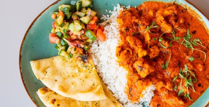 Plate with chicken curry, rice, flatbread, and chopped salad on a turquoise serving dish.