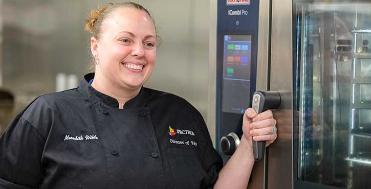 Chef in a commercial kitchen smiling while holding the handle of a Rational Combi oven.