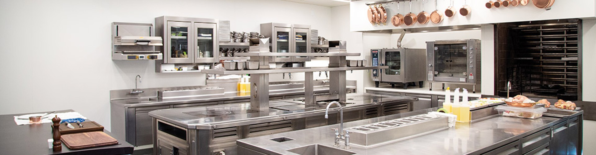 Interior of a professional kitchen with stainless steel equipment, multiple ovens, and a prep area with various ingredients laid out.