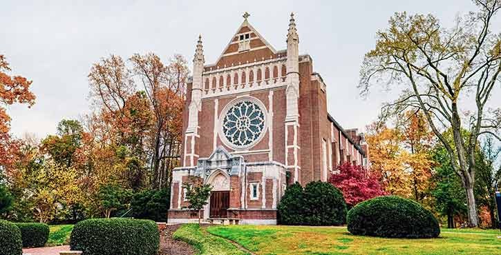 Exterior view of the University of Richmond Chapel with its distinctive large rose window and Gothic architectural elements, surrounded by lush greenery.