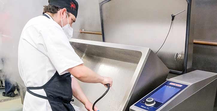 A chef in a commercial kitchen cleans a RATIONAL VarioCookingCenter.