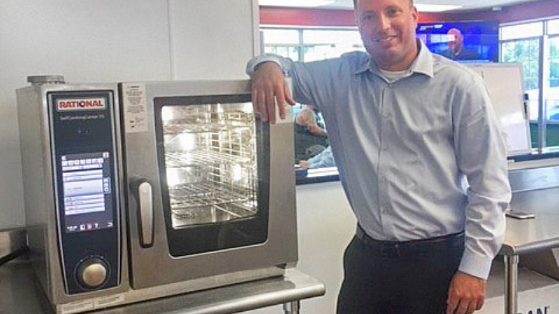 Person standing beside a Rational commercial oven in a showroom setting.