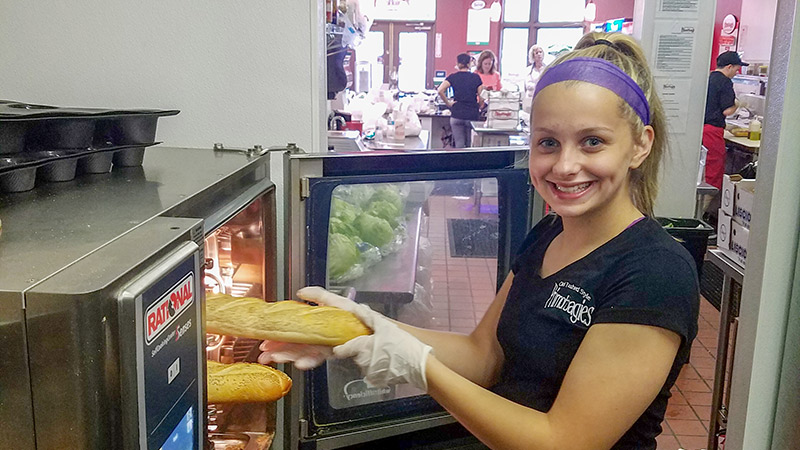 A smiling employee placing bread into an Rational oven.