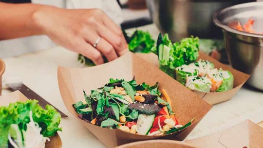 Hand preparing fresh salads in sustainable bowls for catering.
