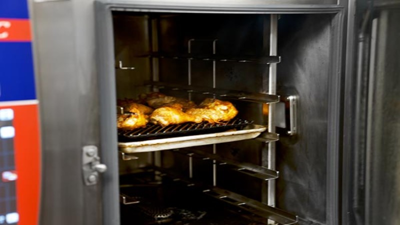 Chicken pieces cooking on rack inside professional combi oven in commercial kitchen.
