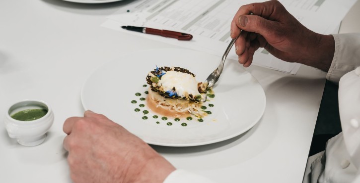 Juge goûtant un plat raffiné avec œuf poché, points de sauce et fleurs comestibles.