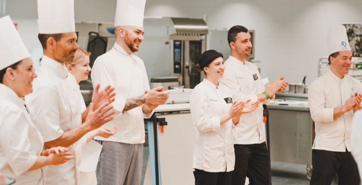 Groupe de chefs en tenue blanche applaudissant dans une cuisine professionnelle.