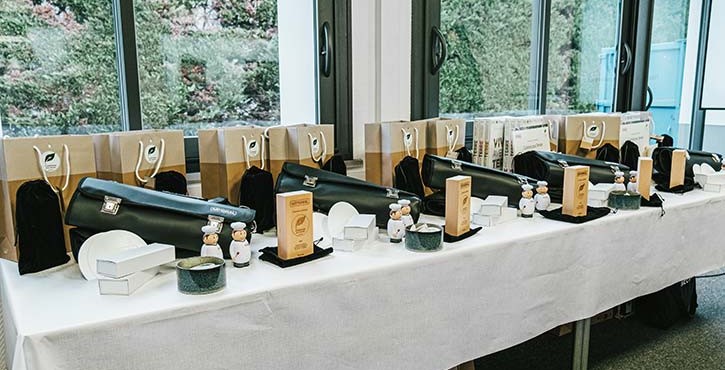 Table de remise de prix avec sacs cadeaux, trophées et figurines de chef près de grandes fenêtres.