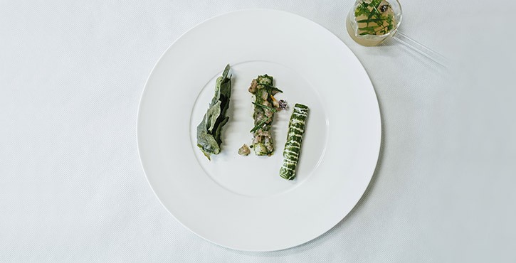 Assiette gastronomique avec légumes et herbes dressés avec soin sur nappe blanche.