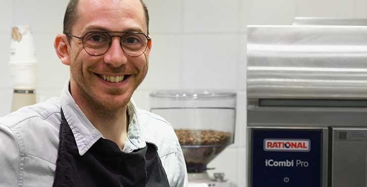Chef souriant à côté d’un RATIONAL iCombi Pro four mixte dans une cuisine professionnelle.
