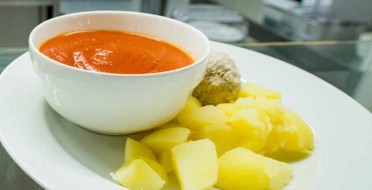 Plate with tomato soup, boiled potatoes and a meatball in a professional kitchen.