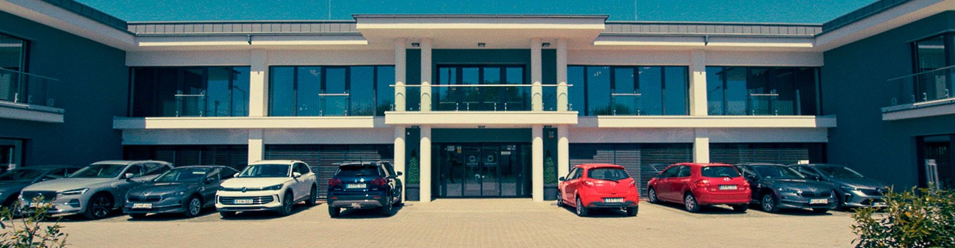 Modern two-storey office building with parked cars in front under a clear blue sky.