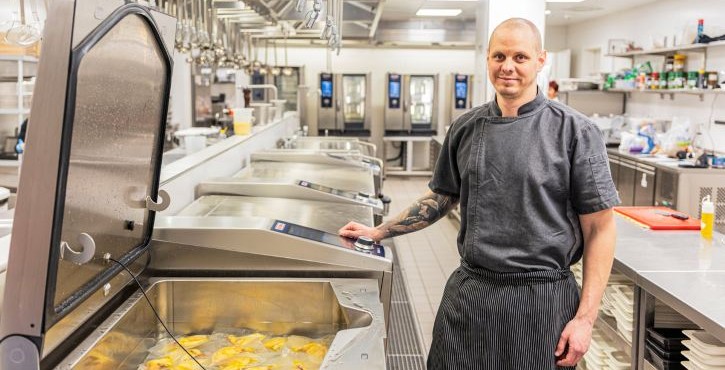 Chef standing beside an open RATIONAL iVario Pro with food in a professional kitchen.