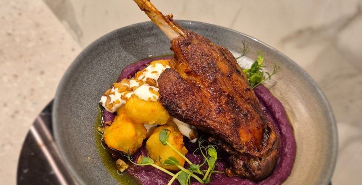 Crispy duck leg with purple purée, golden dumplings and microgreens on grey plate.