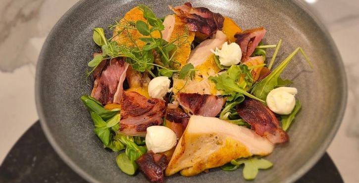 Roasted poultry breast with crispy bacon, pumpkin, greens and herb cream on grey plate.