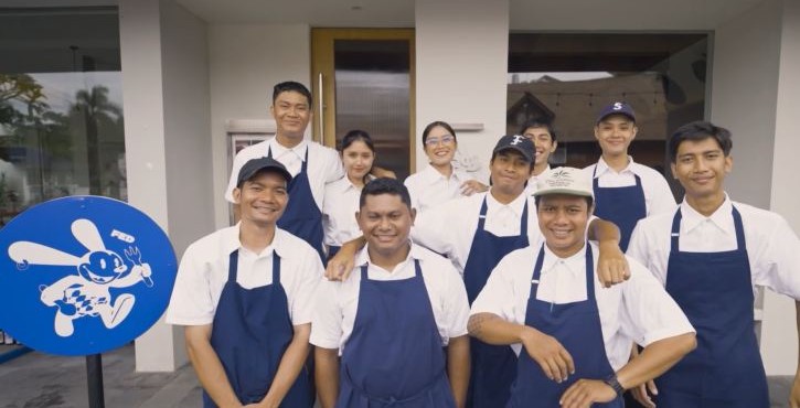 Team of restaurant staff in aprons posing outside building entrance.