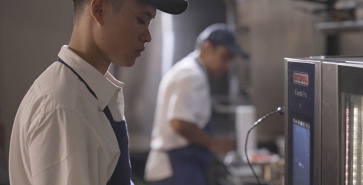 Kitchen staff member operating a RATIONAL iCombi Pro combi oven in a professional kitchen.