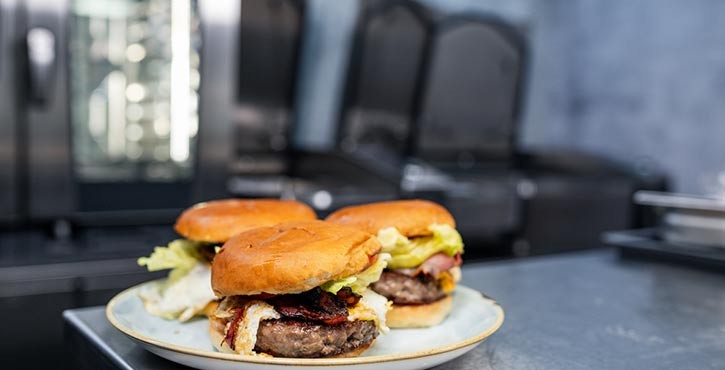 A plate of freshly made burgers with lettuce, bacon, and patties in front of the Rational iCombi Pro ovens.