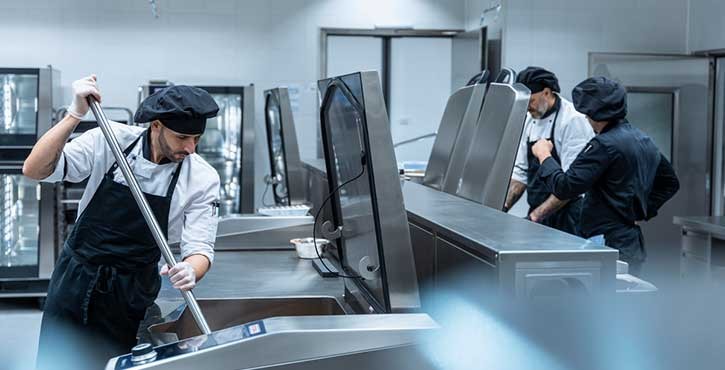 Троє кухарів працюють на професійній кухні з кухонним обладнанням Rational, один з них помішує ложкою.