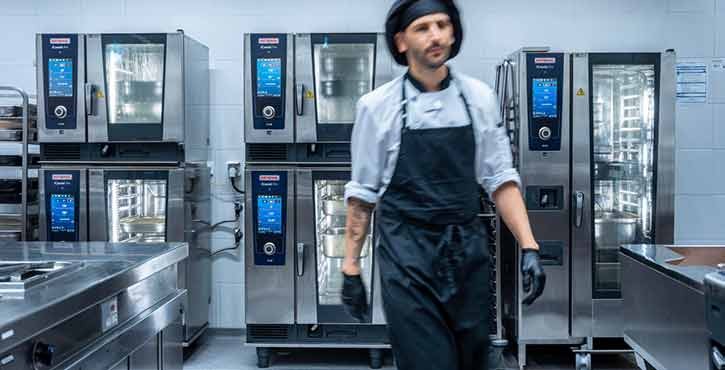 A chef walking past multiple Rational combi-steam ovens in a modern kitchen.