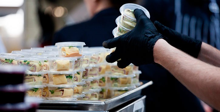 A person wearing black gloves stacking packaged small meals.
