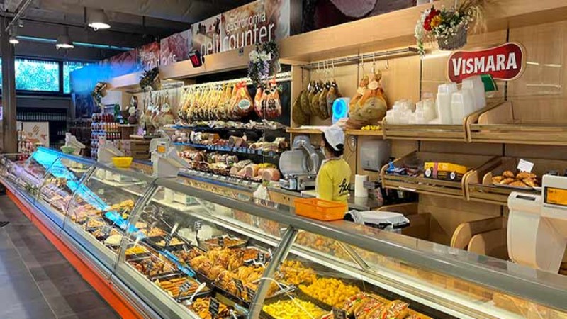 Banco gastronomia con piatti pronti, salumi e prodotti da forno in un mercato alimentare italiano.
